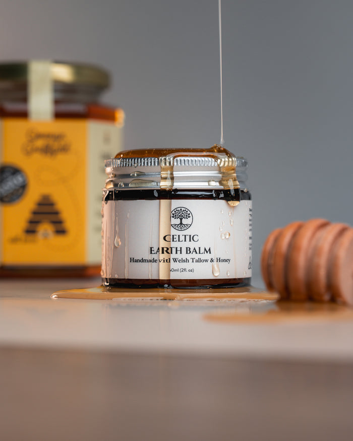 Jar of Celtic Earth Welsh Tallow and Honey Balm with a honey dipper on a gray surface